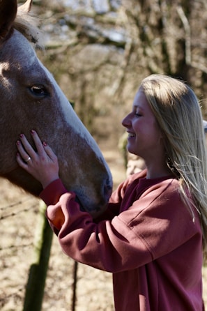 Smiling customer wearing Noble Gallop scarf while grooming her horse outdoors