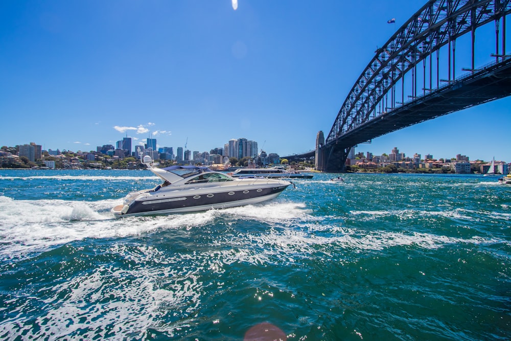 white and gray speedboat running under bridge during daytime