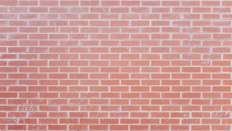 A red brick wall with a consistent pattern, comprising uniformly shaped rectangular bricks and visible mortar lines. Some bricks have slight variations in color and texture, suggesting natural imperfections and wear.