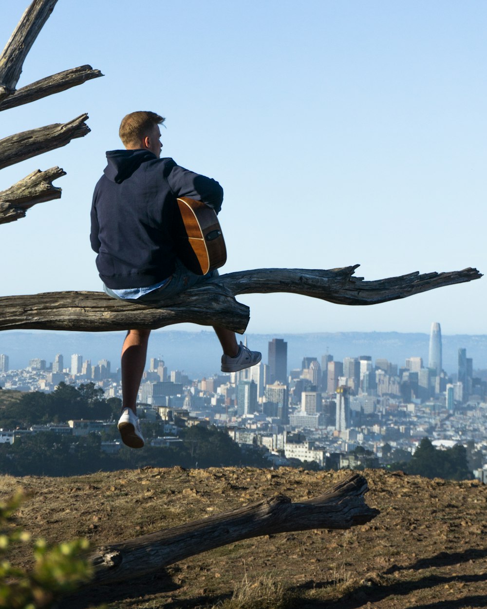 man playing guitar while sitting on log