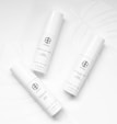 Three white cylindrical skincare product bottles are arranged on a white background with subtle leaf patterns. Each bottle has minimalist black text and logos, conveying a clean and modern aesthetic.