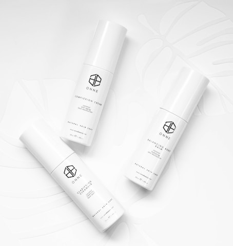 Three white cylindrical skincare product bottles are arranged on a white background with subtle leaf patterns. Each bottle has minimalist black text and logos, conveying a clean and modern aesthetic.