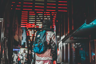 A nighttime cityscape with neon red highlights illuminating a matte black streetwear jacket on an urban rooftop.