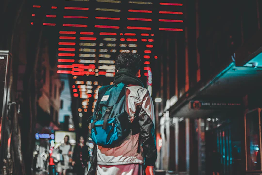 A nighttime cityscape with neon red highlights illuminating a matte black streetwear jacket on an urban rooftop.