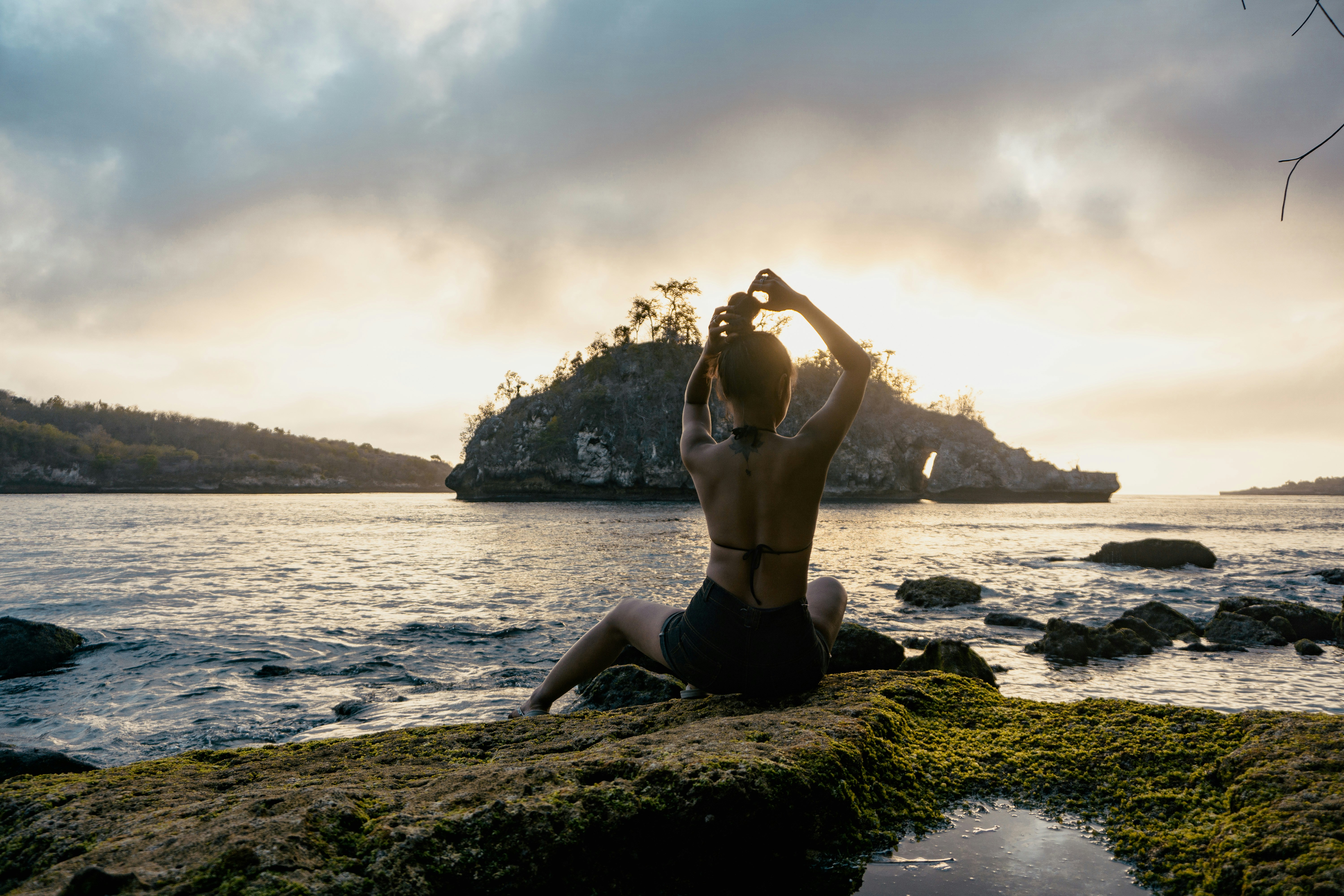 woman sitting on rock formation facing the beach
