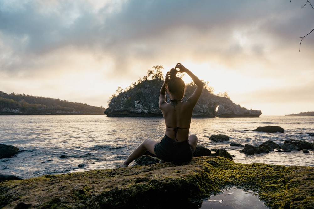 woman sitting on rock formation facing the beach