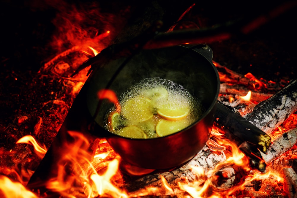 Dutch Oven auf brennendem Feuerholz mit Wasser und Obstscheiben