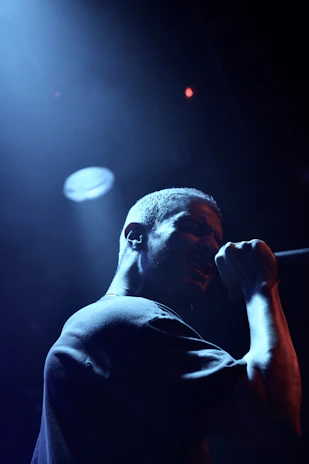 Jai Reign performing on stage under deep purple and gold lighting, eyes closed, pouring emotion into the microphone.