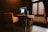 A modern office space featuring a wooden desk with a large monitor and a sleek computer setup. An orange upholstered chair is positioned in front of the desk. There is soft lighting and a window with horizontal blinds, casting a warm ambiance.