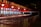 A row of ticket booths under a red and white striped canopy is lit with warm lights. The booths display digital screens and are arranged along metal railings. The scene is illuminated in a night setting with an empty path leading towards the booths.