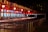 A row of ticket booths under a red and white striped canopy is lit with warm lights. The booths display digital screens and are arranged along metal railings. The scene is illuminated in a night setting with an empty path leading towards the booths.