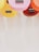 Several colorful ukuleles are arranged with their bodies facing downward. They are in vibrant shades of pink, yellow, orange, and red, and their black bridges and white strings are visible. The clean, light background enhances the brightness of the ukuleles.