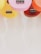Several colorful ukuleles are arranged with their bodies facing downward. They are in vibrant shades of pink, yellow, orange, and red, and their black bridges and white strings are visible. The clean, light background enhances the brightness of the ukuleles.