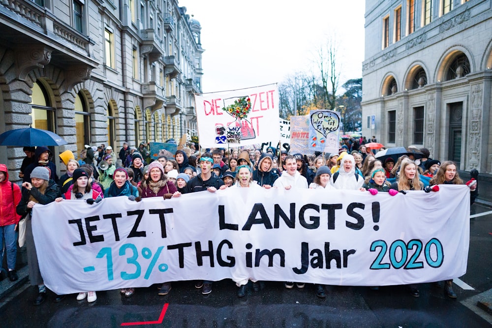 people holding banner on road between buildings during daytime