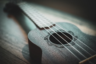 A close-up of hands strumming a ukulele with sheet music in the background.
