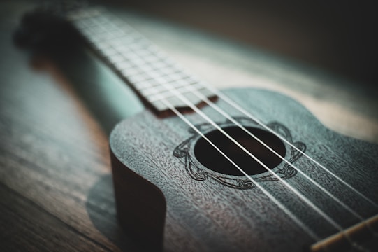 Close-up of a hand strumming a wooden ukulele with warm sunlight filtering through a window.