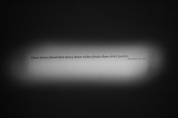 A quote is displayed on a textured surface with a spotlight effect highlighting the text. The quote reads, 'I have always found that mercy bears richer fruits than strict justice.' attributed to Abraham Lincoln. The background is dark, drawing attention to the quote centered in the light.