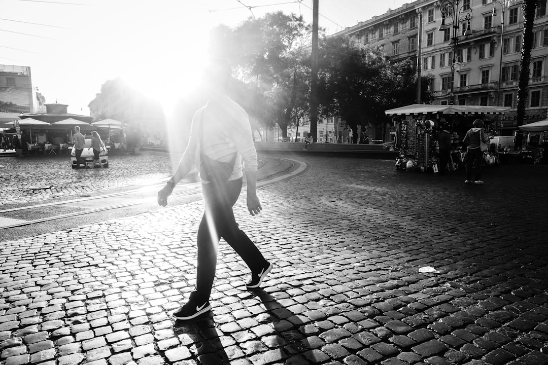 grayscale photo of man walking on brick pavement