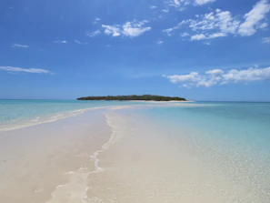 A serene secret island beach with crystal-clear turquoise water and soft white sand under a bright blue sky.