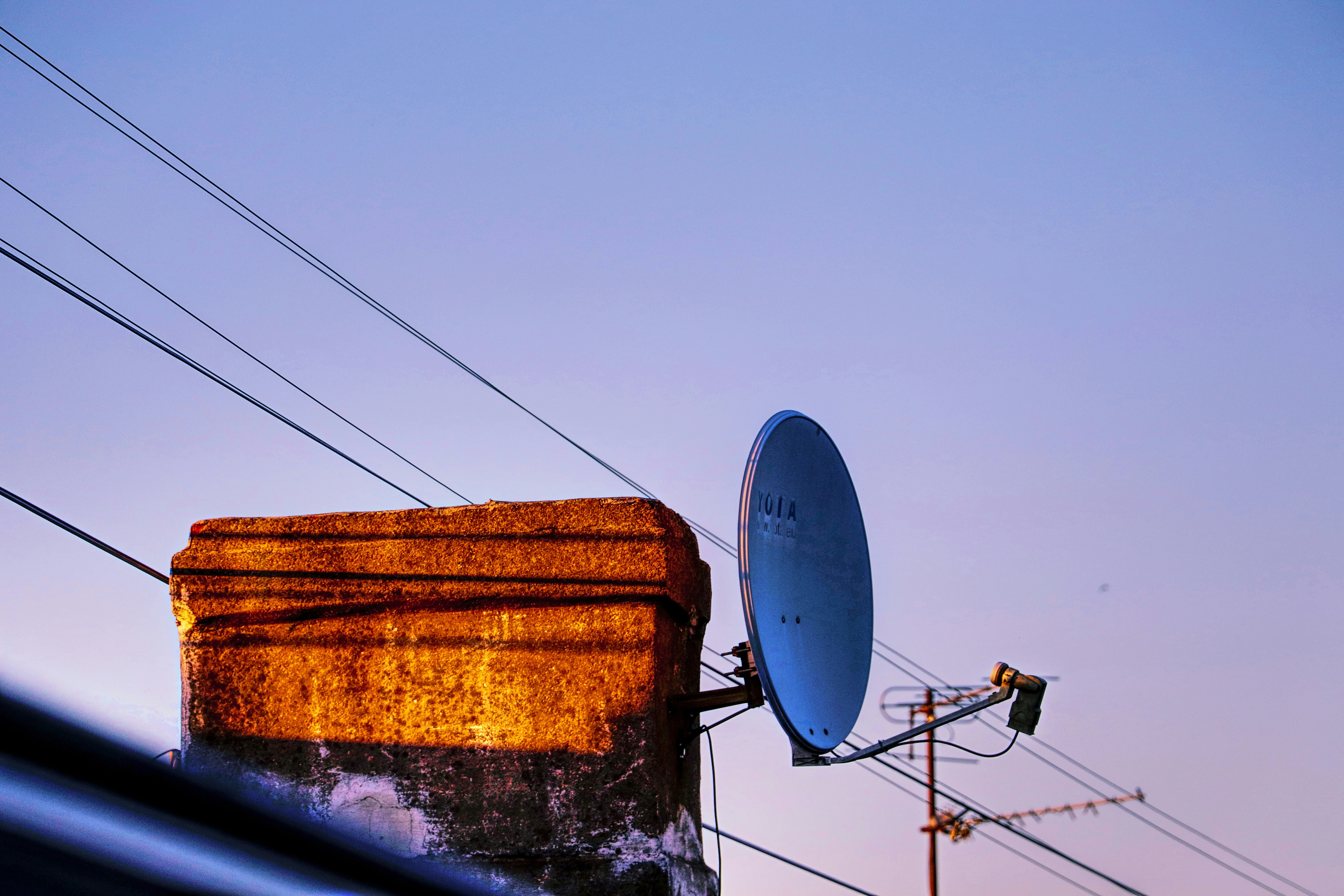 antena parabólica blanca en foco, atrás contiene un poste de energía con cables y el cielo de fondo.