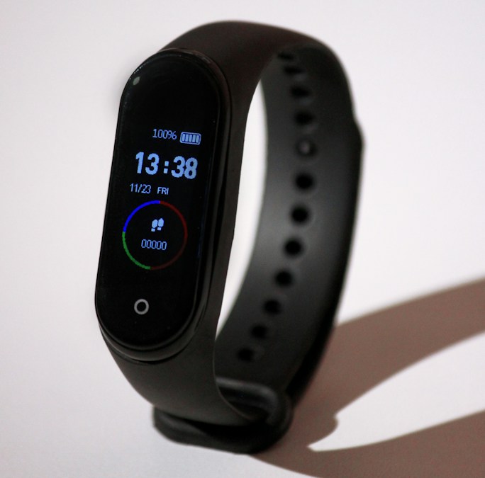 Bracelet connecté noir à l'écran allumé affichant l'heure et le niveau de batterie, en illustration
