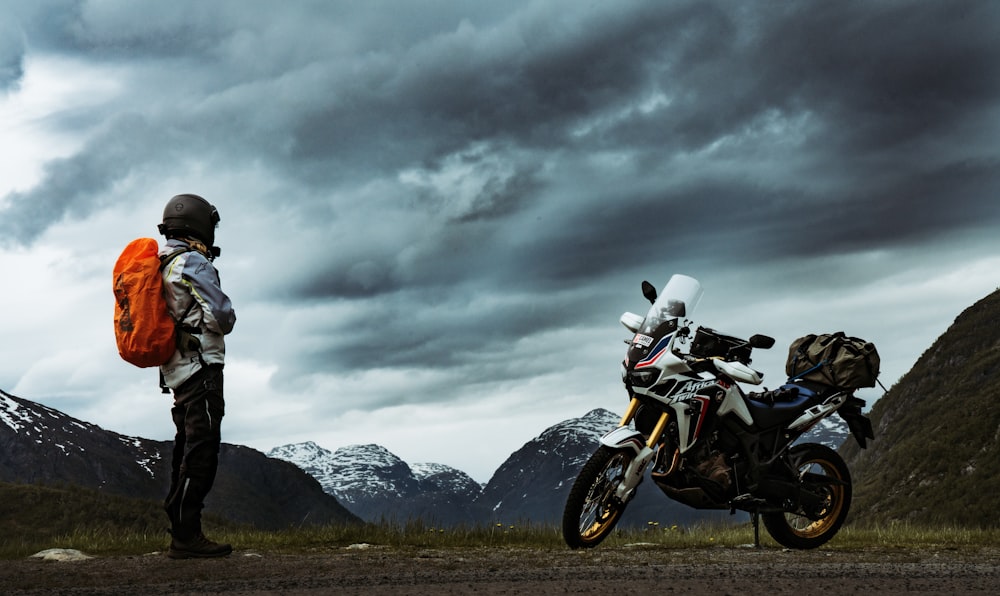 man standing in front of park motorcycle near snow-covered mountain during daytime