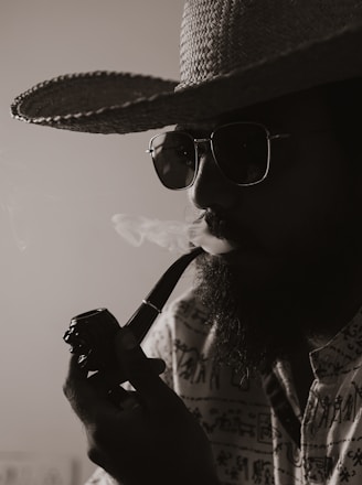 a man in a hat and sunglasses smoking a pipe