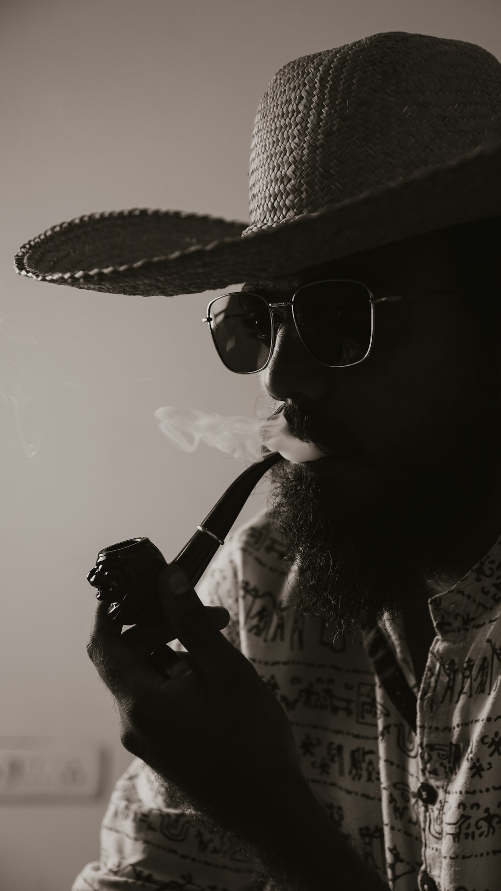 a man in a hat and sunglasses smoking a pipe