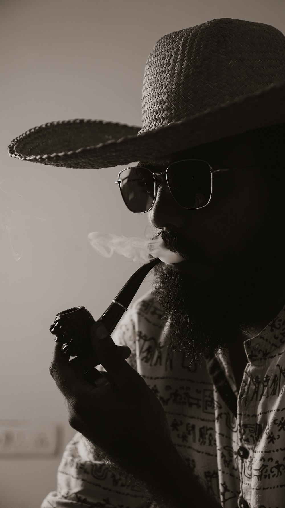 Un homme avec un chapeau et des lunettes de soleil fumant la pipe
