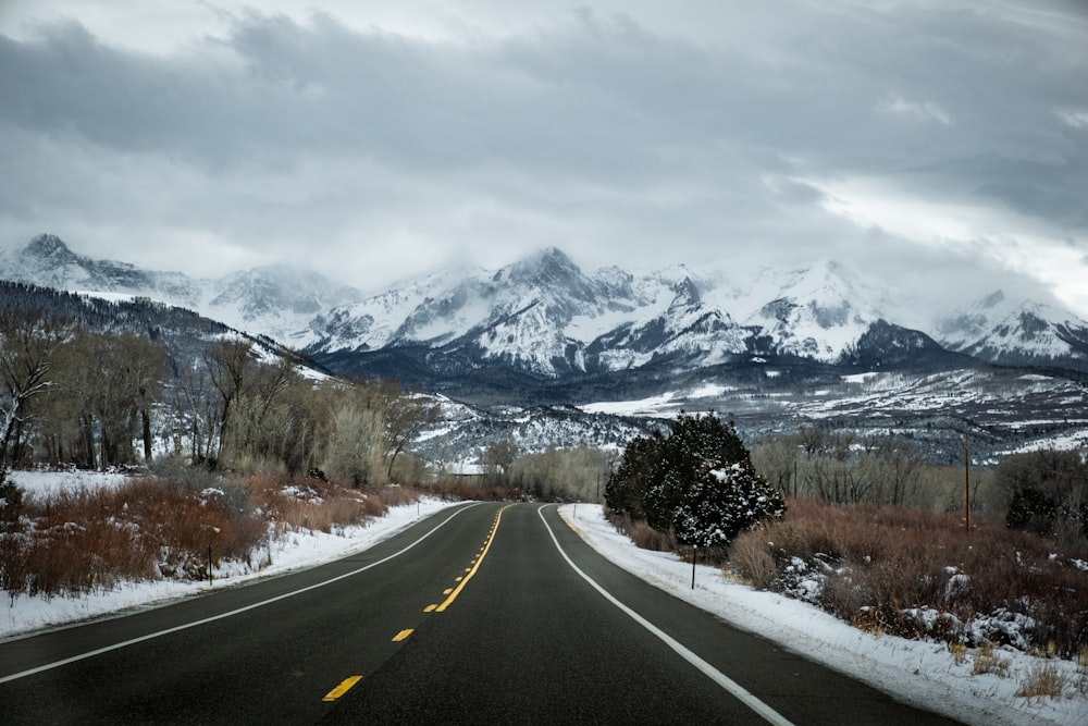 gray road with no vehicle viewing mountain covered with snow under white and blue sky during daytime