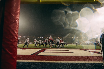 A close-up of a football spiraling through the air toward the end zone under bright stadium lights.