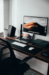 A home office workspace with a laptop, monitor, and keyboard on a wooden desk