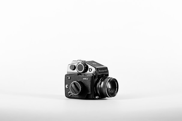 Sleek black medium format camera with leather grip displayed against a soft fabric backdrop.
