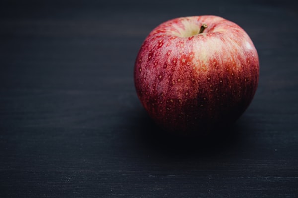 A ripe red apple on a dark wooden surface