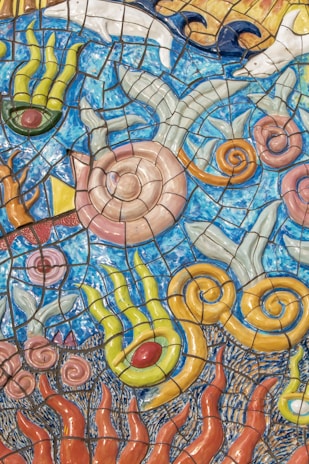 Colorful mosaic art depicts swirling patterns resembling underwater sea life with abstract shapes. The artwork features vibrant tiles in blue, yellow, green, and orange, with designs that mimic seashells, seaweed, and waves.