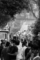 A crowd of people, some wearing face masks and gloves, gathered around a truck amidst debris and trees. Their raised fists suggest a sense of protest or solidarity.