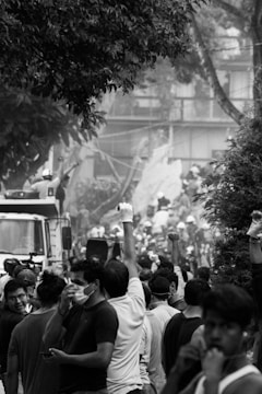A crowd of people, some wearing face masks and gloves, gathered around a truck amidst debris and trees. Their raised fists suggest a sense of protest or solidarity.