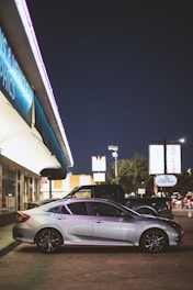 A sleek black tow truck hauling a silver sedan on a city street at dusk.