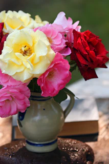 A close-up of vibrant roses and ranunculus arranged in a rustic ceramic vase, glowing in gentle morning light.