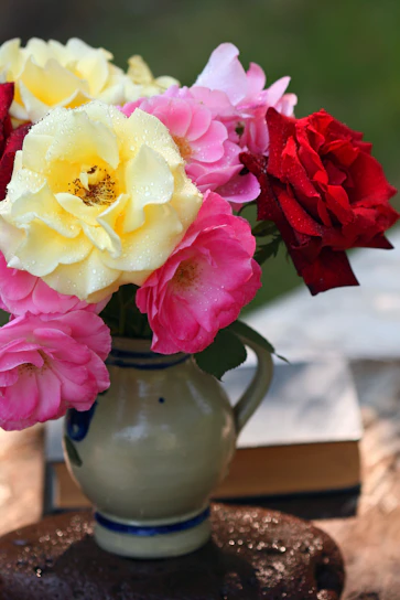 A close-up of vibrant roses and ranunculus arranged in a rustic ceramic vase, glowing in gentle morning light.