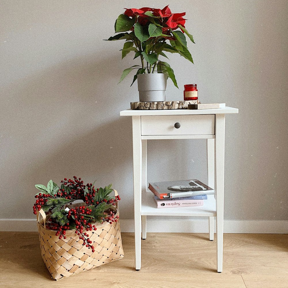 poinsettia flowers on top of white wooden end table and berries wreath on basket