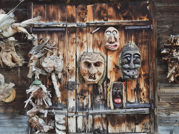 Hand-carved wooden masks arranged against a textured wall, each telling a unique story.