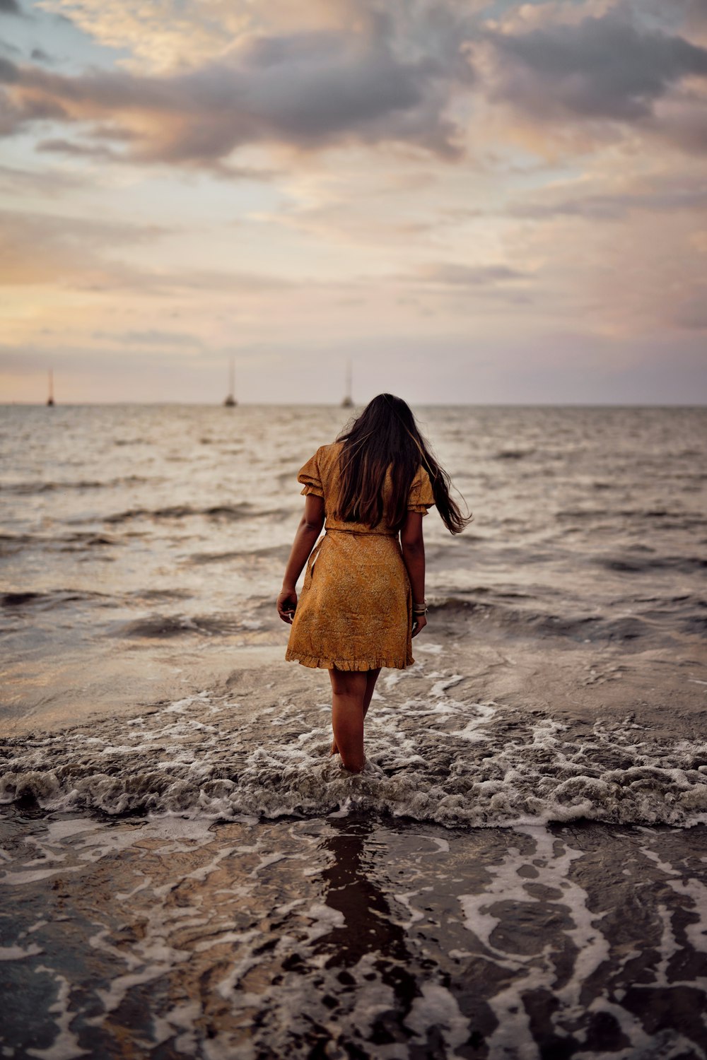 woman wearing yellow dress standing on seashore under white and gray sky