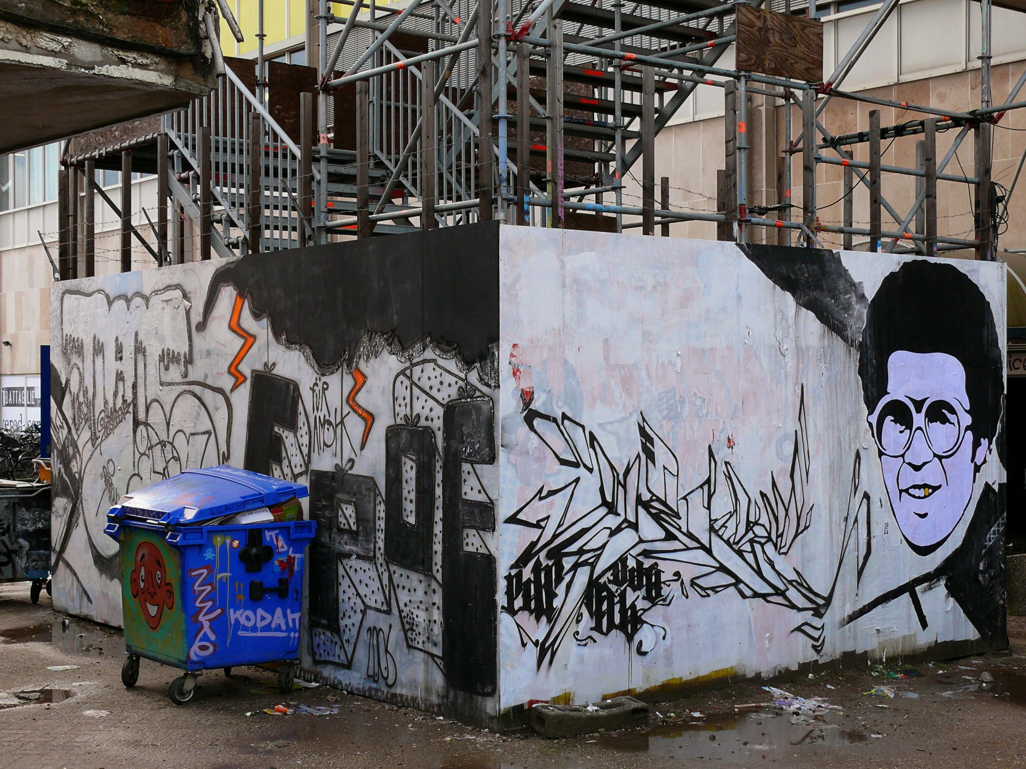 Wall painting, graffiti and glued stencil art, painted on a wooden construction fence in Amsterdam City, located in building activities in the area of Oosterdoks Eiland - now the new location if the Booking.com building. This place was close to the now demolished head Post Office building of Amsterdam city; free images of street photography of urban art by Fons Heijnsbroek, urban photography of The Netherlands.