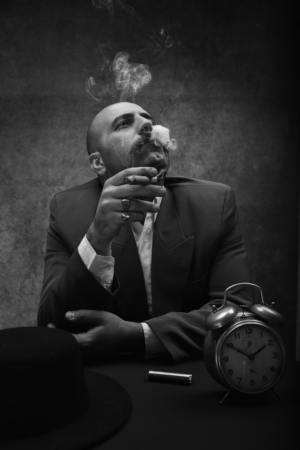 man wearing black suit sitting by the table while smoking