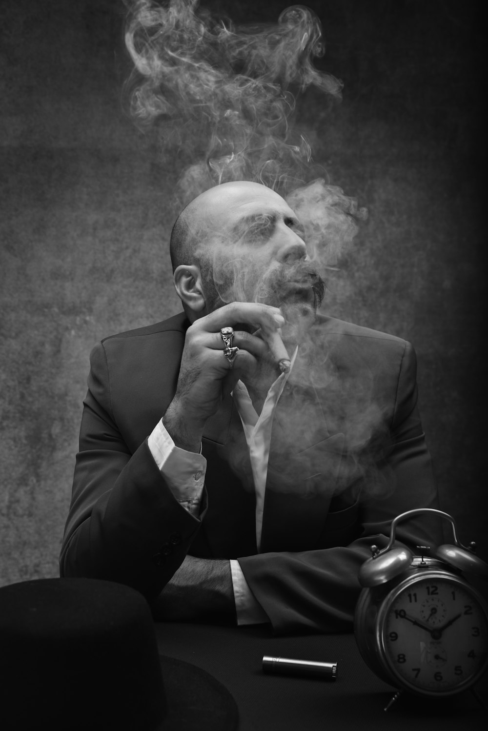 man wearing black suit sitting by the table smoking