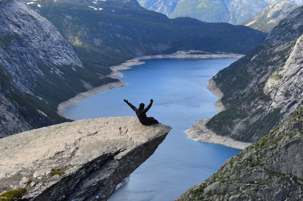 Person, die tagsüber auf einem Felsen in der Nähe eines Gewässers sitzt