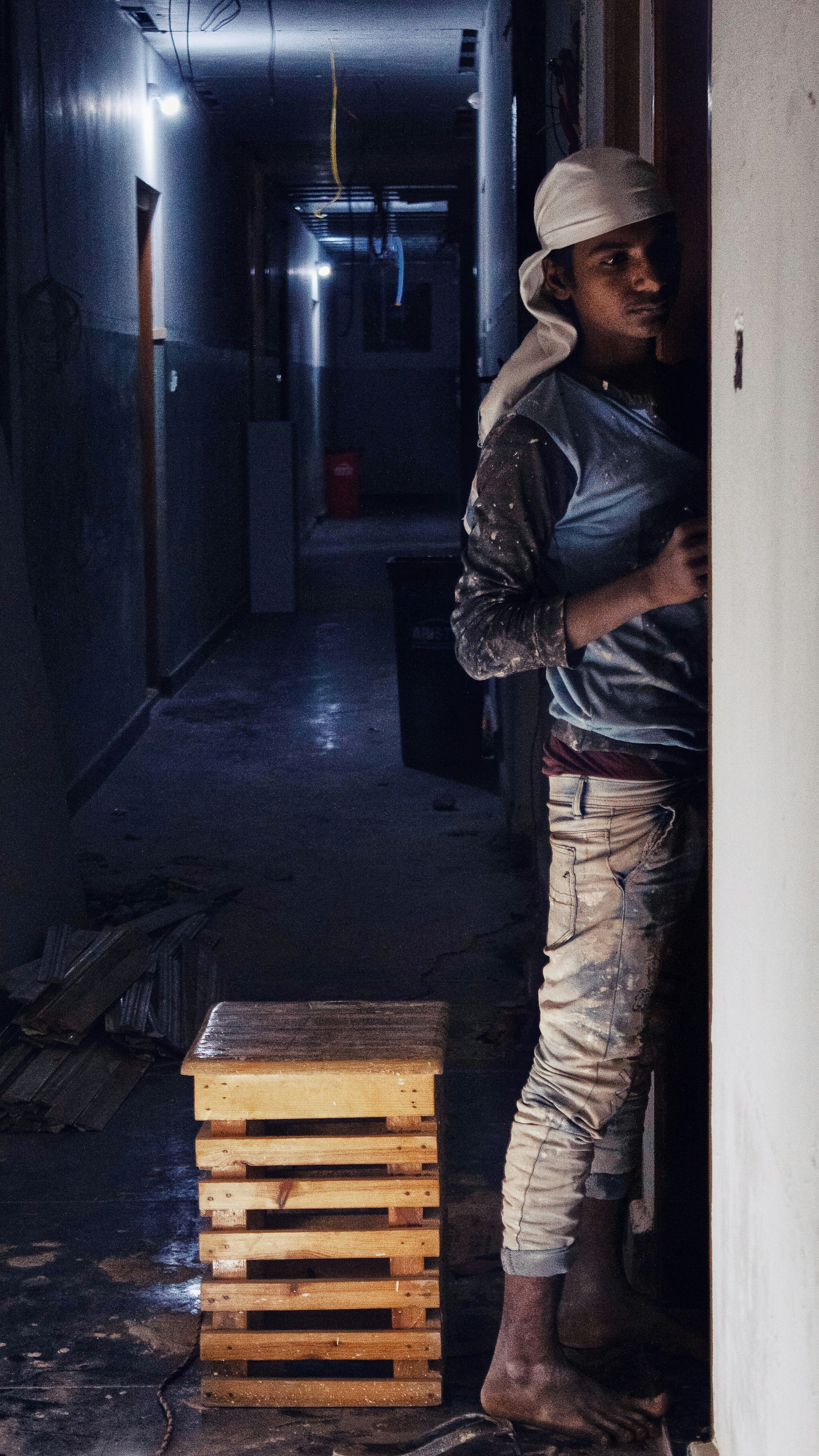man wearing blue long-sleeved shirt wearing white hat leaning on wall