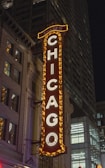 A large vertical marquee with bright lights displays the word CHICAGO in capital letters, attached to a historic building. The architecture features decorative elements, and the night setting emphasizes the illuminated sign.