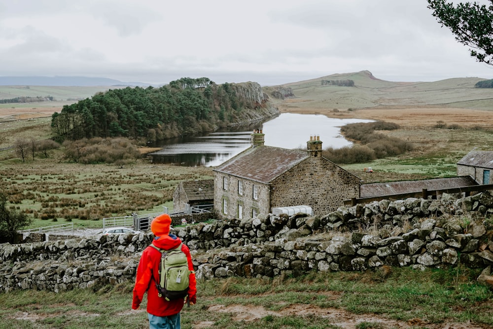 person wearing hooded jacket walking on green grass near stone fence during daytime